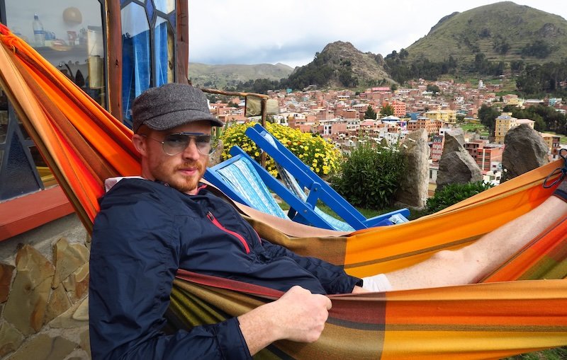 Nomadic Samuel enjoying the relaxed life in Copacabana, Bolivia wearing jacket, hat and sunglasses on South America backpacking trip 