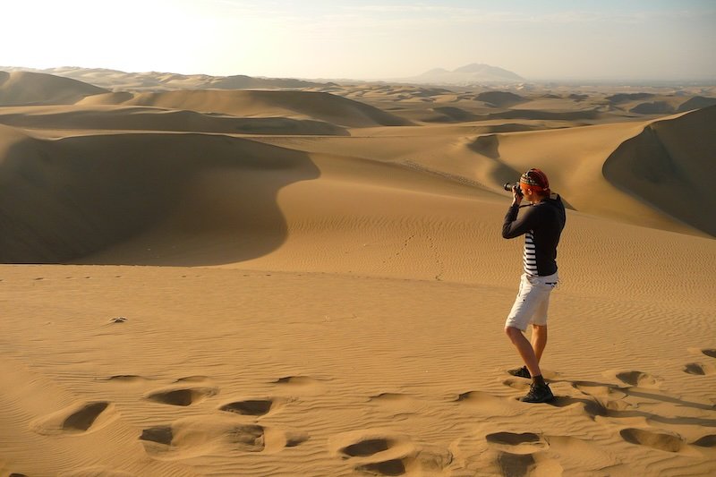Nomadic Samuel photographing sand dunes in Huacachina, Peru’s desert oasis, capturing iconic travel photography moments