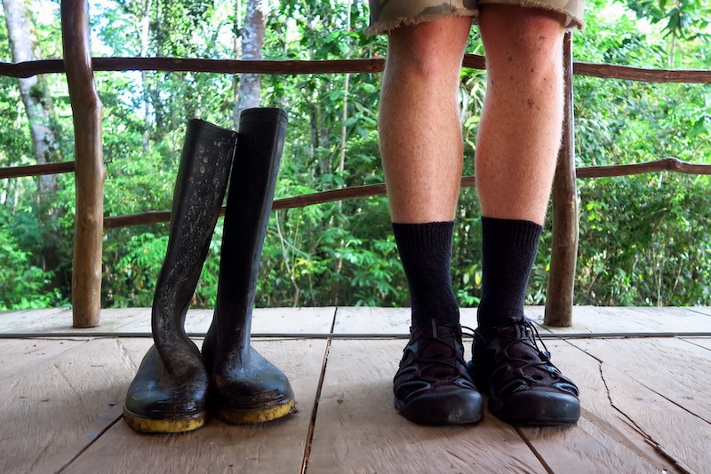 Nomadic Samuel wearing shorts, socks and crocs next to serious jungle worthy rubber boots as part of the packing for the Amazon essentials 