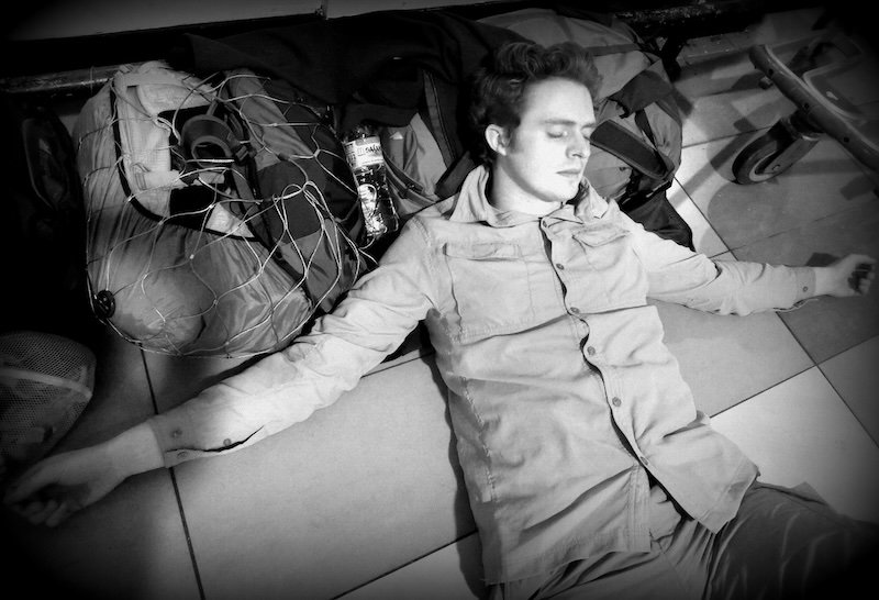 Nomadic Samuel sleeping blissfully with his gear tied up in Kuala Lumpur, Malaysia at the airport Nomadic Samuel sleeping blissfully with his gear tied up in Kuala Lumpur, Malaysia at the airport