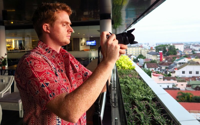 Nomadic Samuel wearing an Indonesian batik shirt taking photos from a high vantage point in Yogyakarta, Indonesia during a nice warm weather day 