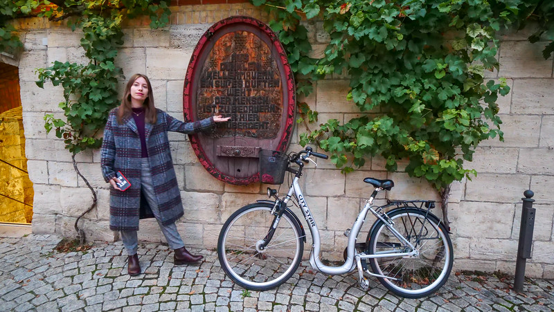 Outside 51° Restaurant & Weinbar in Freyburg with That Backpacker Audrey Bergner pointing towards the logo and bicycle covered in ivy
