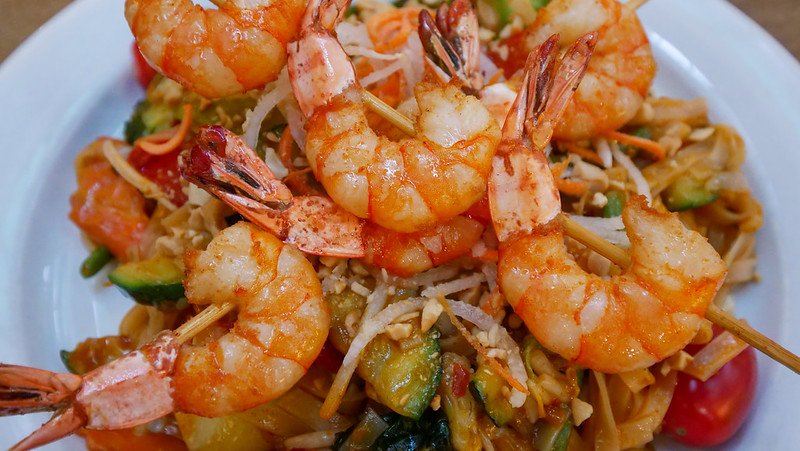 Close-up of a vibrant pad thai topped with grilled shrimp skewers, crunchy vegetables, crushed peanuts, and rice noodles, served at Markthalle Freiburg in Freiburg im Breisgau, Germany