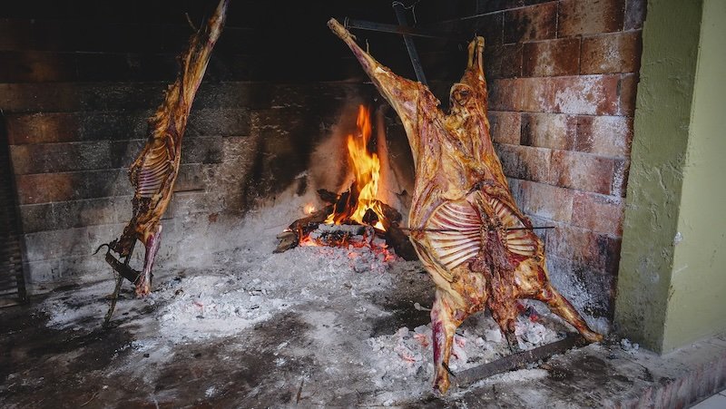 Traditional Patagonian asado with whole cordero (lamb) slow-roasting over open flames on an iron cross grill in Puerto Madryn, Argentina, showcasing a classic culinary experience that highlights regional culture, flavors, and gaucho heritage