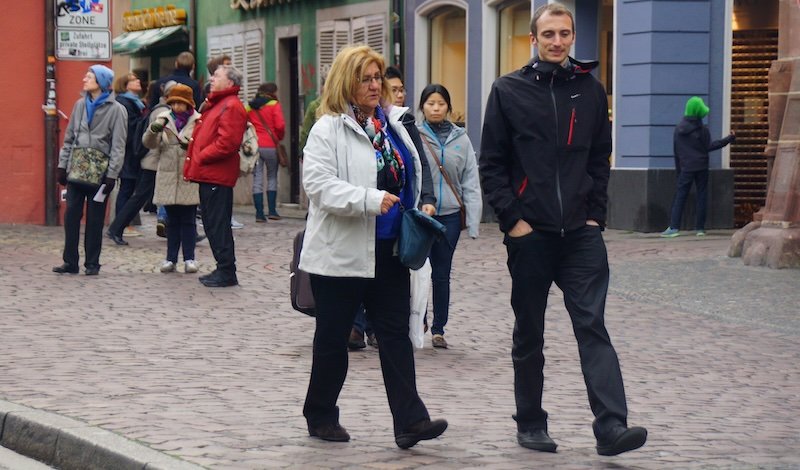 Pedestrians strolling through the cobblestone streets of the historic old town square in Freiburg im Breisgau, Germany, surrounded by colourful traditional buildings