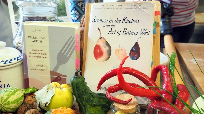 Cookbooks by Pellegrino Artusi, including Science in the Kitchen and the Art of Eating Well, displayed with fresh vegetables and chili peppers in Emilia-Romagna, Italy, celebrating the region’s culinary heritage and influence on Italian gastronomy