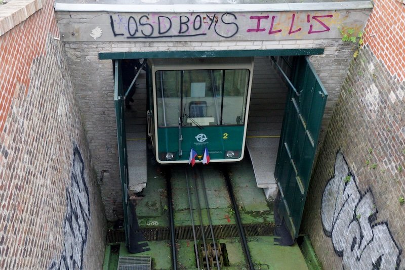 Green funicular car emerging from a graffiti-covered tunnel on the historic Petřín Funicular railway in Prague, Czech Republic, used to reach Petřín Hill