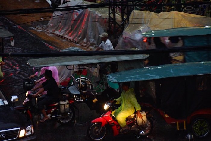 Motorbikes and tuk-tuks navigating the bustling streets of Phnom Penh, Cambodia during a heavy evening rainstorm, showcasing the city’s lively traffic and resilient commuters