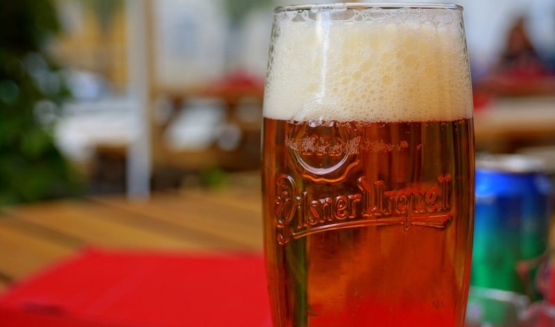 Close-up of a freshly poured glass of golden Pilsner Urquell beer with a frothy head on an outdoor table at a pub in Prague, Czech Republic, showcasing the city’s world-famous beer culture