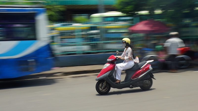 Plan your trip to Vietnam with a local lady on a scooter zooming by in Ho Chi Ming City, Vietnam 