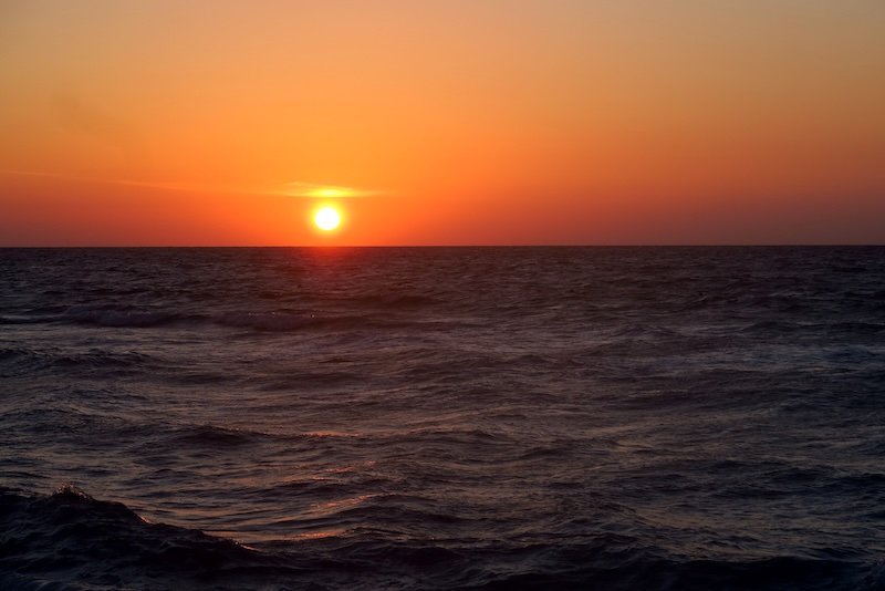 Fiery orange sun setting over the Caribbean Sea, casting a warm glow across gentle waves off the coast of Playa del Carmen, Mexico