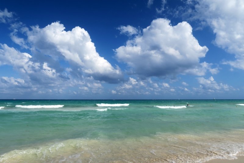 Turquoise waves roll gently onto the golden sands of Playa del Carmen under a sky dotted with fluffy white clouds, capturing the serene tropical beauty of the Mexican Caribbean coastline Turquoise waves roll gently onto the golden sands of Playa del Carmen under a sky dotted with fluffy white clouds, capturing the serene tropical beauty of the Mexican Caribbean coastline