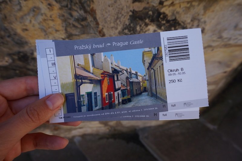 Close-up of a hand holding entrance tickets for Prague Castle featuring a colorful photo of Golden Lane, one of the highlights inside the castle complex in Prague, Czech Republic
