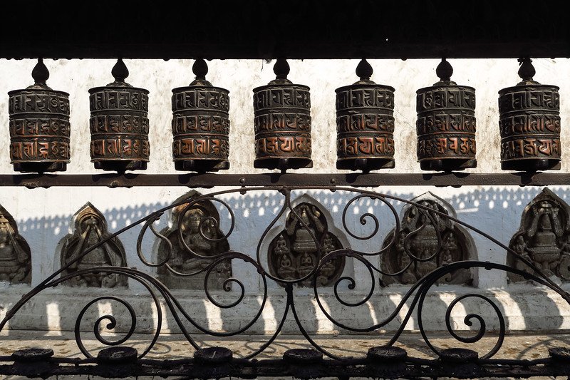 Row of bronze prayer wheels inscribed with mantras at Swayambhunath Stupa in Kathmandu, Nepal, a sacred Buddhist site where pilgrims spin the wheels for blessings and spiritual merit