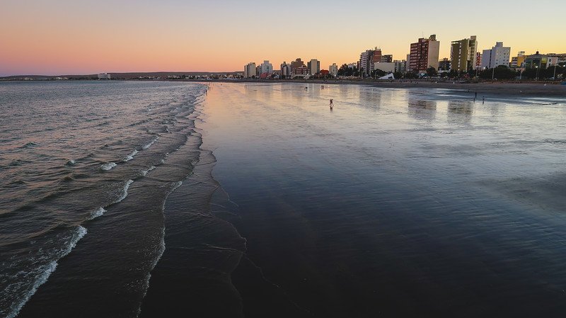 Sunset views from the pier in Puerto Madryn, Patagonia, Argentina, with pastel skies reflecting over the calm shoreline and city skyline. This peaceful evening scene highlights one of the best free activities when visiting Puerto Madryn and Peninsula Valdes