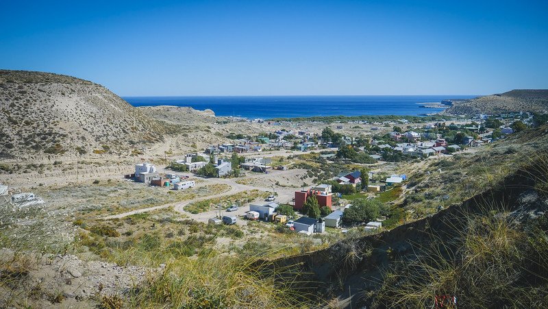 Panoramic view of Puerto Pirámides on Península Valdés, Argentina, captured from a high vantage point surrounded by rugged hills and overlooking the sparkling blue waters of the Golfo Nuevo — a scenic approach to this charming Patagonian coastal village