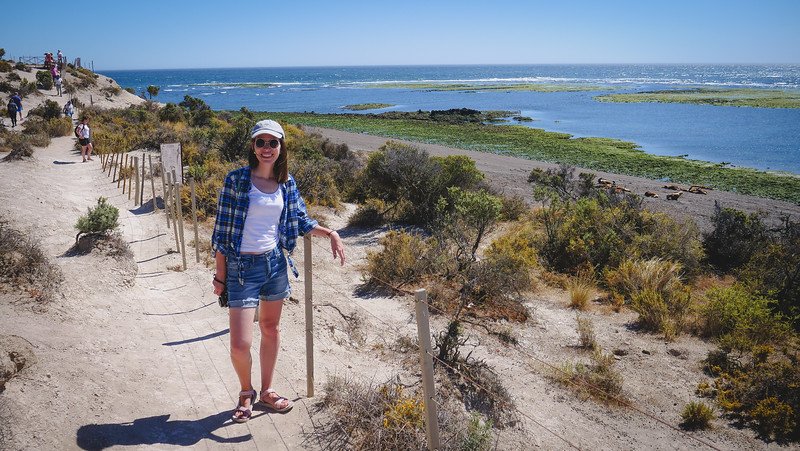 Audrey Bergner of That Backpacker stands on a sandy trail overlooking the coast at Punta Norte on Península Valdés, Argentina. This area is known for its wildlife, including sea lions and orcas, and offers scenic coastal walks with panoramic ocean views