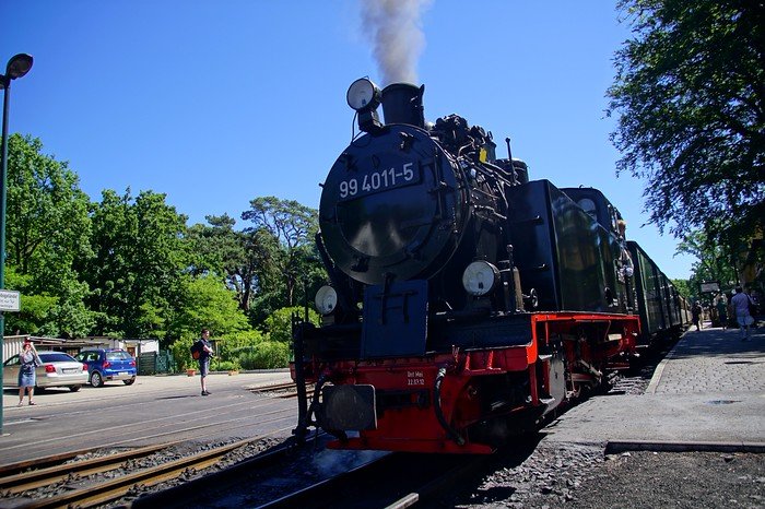 Historic Rasender Roland steam locomotive releasing white smoke as it prepares to depart a rural station on Rügen Island, Germany, offering a nostalgic train ride through scenic Baltic landscapes