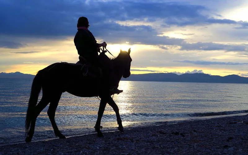 Riding on the shores of Song Kol, Kyrgyzstan during sunset with the horse and rider as a silhouette 