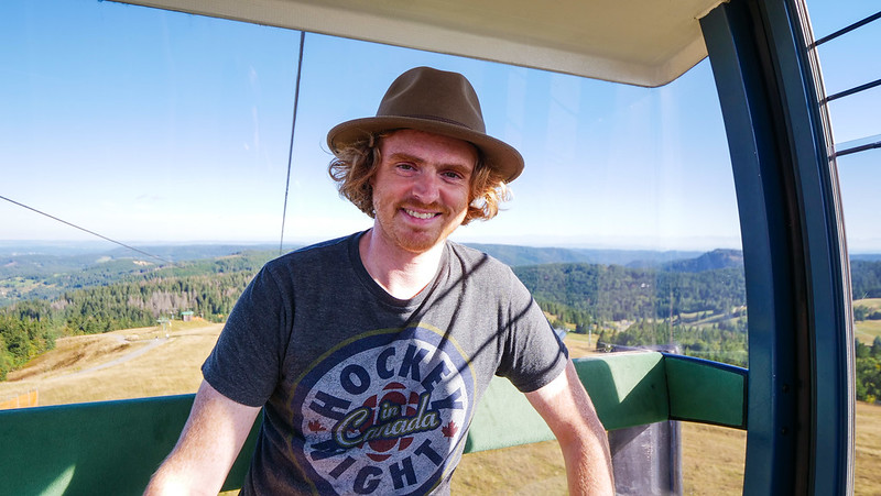 Riding the Feldberg cable car in Germany's Black Forest with Nomadic Samuel smiling and enjoying the epic views whilst wearing a distinct hat