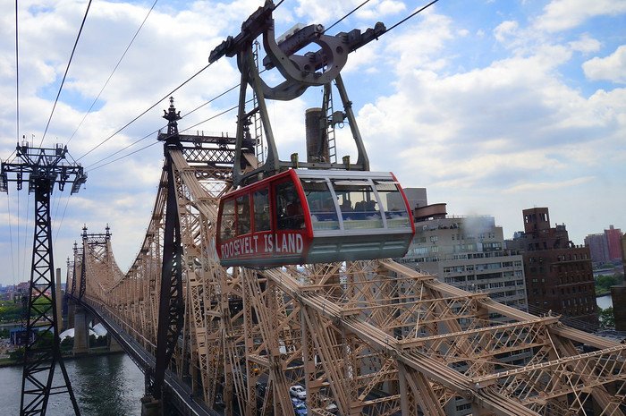 The Roosevelt Island Tram glides above the East River alongside the Queensboro Bridge, offering panoramic views of Manhattan’s skyline and the water below. This iconic red aerial tramway connects Roosevelt Island to Midtown Manhattan, making for a scenic NYC ride