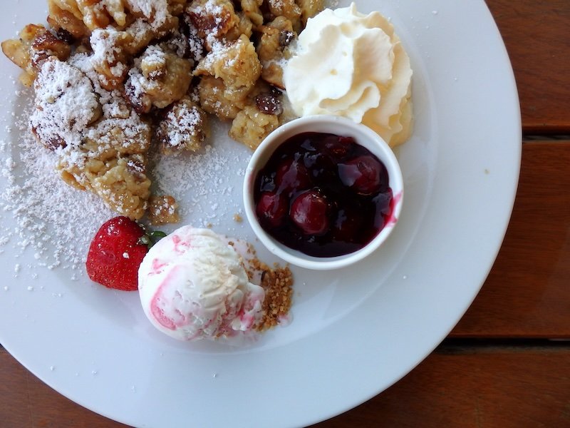 Traditional German dessert enjoyed on Rügen Island, Germany, featuring fluffy Kaiserschmarrn dusted with powdered sugar, served with whipped cream, vanilla ice cream, cherry compote, and a fresh strawberry