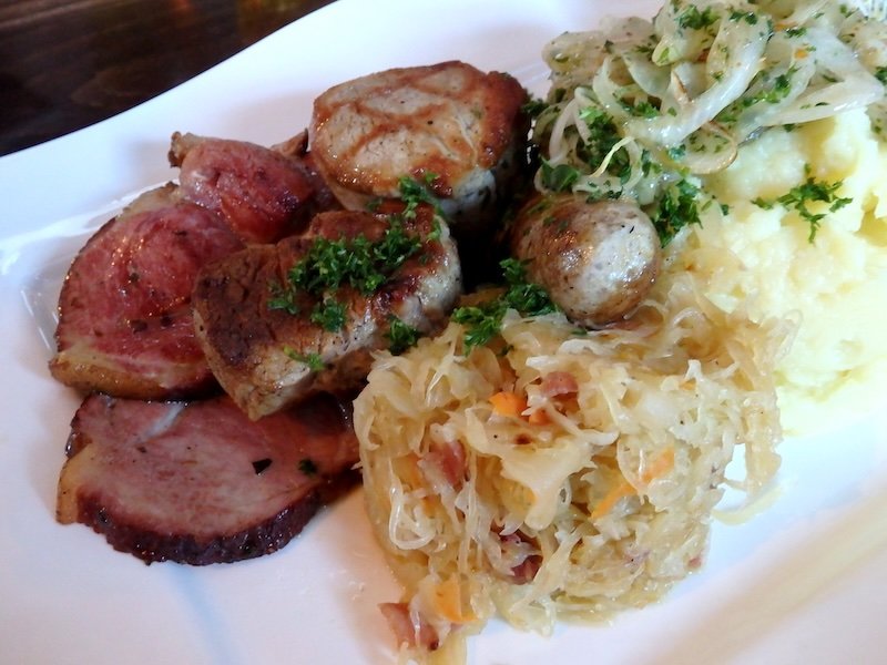 Hearty traditional German meal served on Rügen Island, Germany, featuring assorted grilled sausages, roasted pork medallions, smoked ham slices, sauerkraut, mashed potatoes, and fresh herb garnish