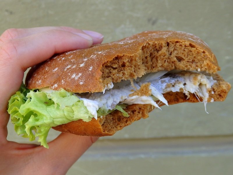 Close-up of a traditional herring sandwich on Rügen Island, Germany, featuring marinated herring fillet, fresh lettuce, and crusty rye bread, showcasing the island’s Baltic Sea seafood cuisine
