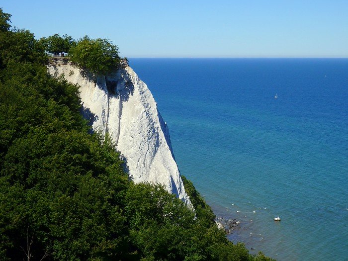 Dramatic white chalk cliffs of Rügen Island in Germany rising above the turquoise waters of the Baltic Sea, framed by lush green forest under a clear summer sky