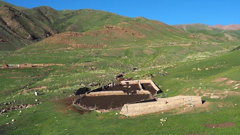 A small remote farmstead with stone animal pens nestled in the rolling green hills of rural Kyrgyzstan, seen during the 3-Day Panorama Trek