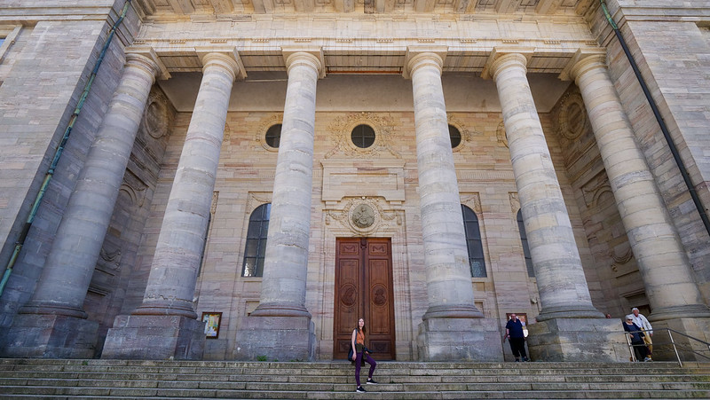 Saint Blaise Cathedral in Germany's Black Forest with its impressive columns wide angle views with That Backpacker Audrey Bergner posing to highlight its grand perspective
