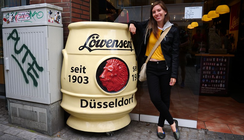 Sampling some mustard at Löwensenf in Düsseldorf, Germany with That Backpacker Audrey Bergner posing outside