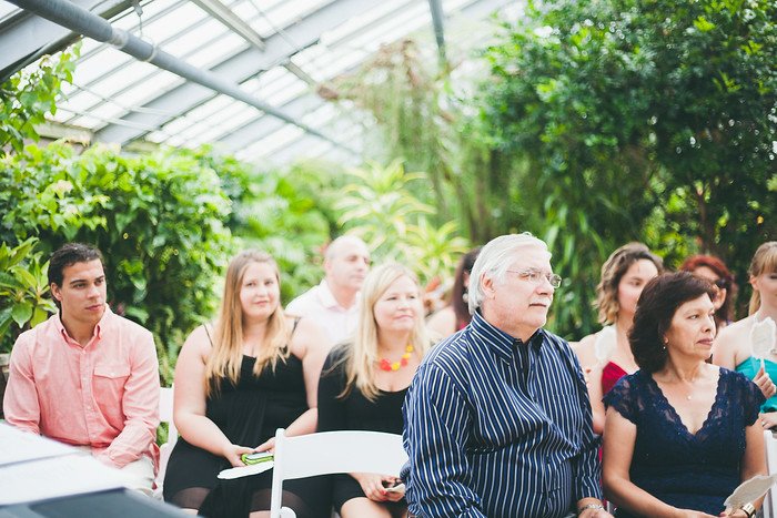 Guests seated inside the lush tropical greenhouse venue during Samuel and Audrey’s summer wedding in Brampton, Ontario. Family and friends attentively watch the ceremony, surrounded by greenery that enhances the intimate and joyful atmosphere