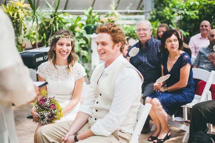Samuel and Audrey share a lighthearted laugh during their summer wedding ceremony in Brampton, Ontario, surrounded by family and friends. Audrey holds a bouquet of wildflowers, and the moment captures their joy and playful spirit as vows are exchanged