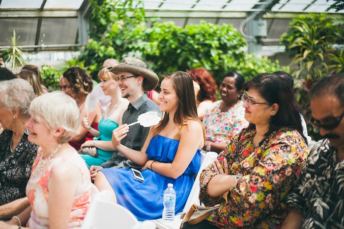 Friends and family seated at Samuel and Audrey’s summer wedding in Brampton, Ontario, enjoying the ceremony inside a lush greenhouse venue. Guests smile and laugh, capturing the joyful and relaxed atmosphere of this intimate celebration