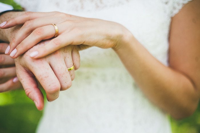 Close-up of Samuel and Audrey’s hands intertwined, showcasing their gold wedding bands on the special day. The delicate lace of Audrey’s dress adds elegance to this symbolic moment of unity, captured during their summer wedding in Brampton, Ontario