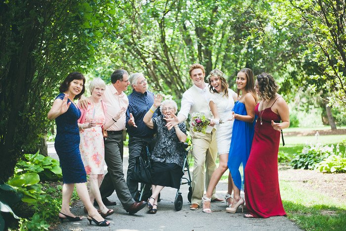 Candid wedding photo of Samuel and Audrey with family and friends in a park in Brampton, Ontario. The group strikes playful poses after the photographer’s cue to “be casual,” capturing a fun and lighthearted moment surrounded by greenery and sunshine