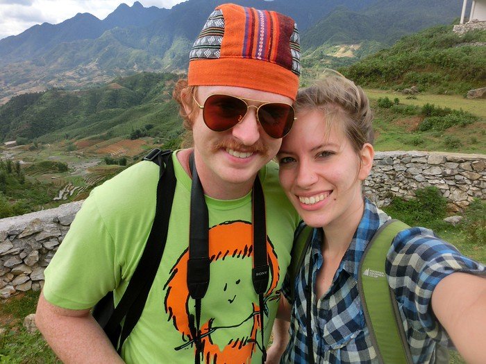 That Backpacker Audrey Bergner and Nomadic Samuel smiling together on a scenic hike in Sapa, Vietnam, with terraced rice fields and lush mountains in the background