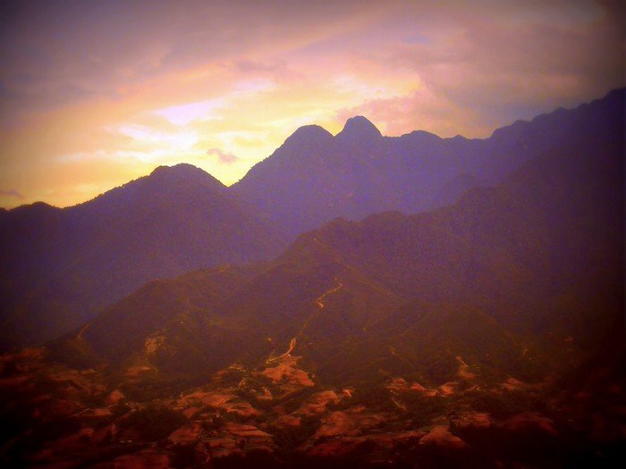 Dramatic sunset over the rugged mountain peaks surrounding Sapa in northern Vietnam, with warm golden light casting a glow on the valleys below