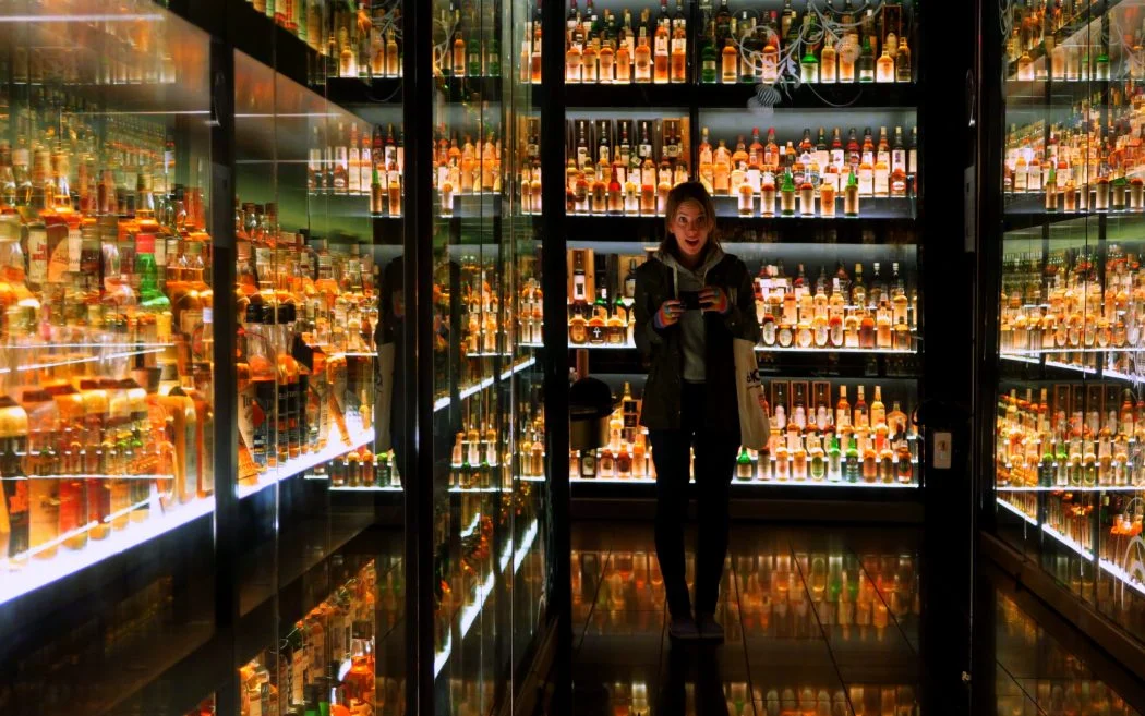 That Backpacker Audrey Bergner inside the Scotch Whisky Experience in Edinburgh, Scotland surrounded by illuminated shelves of rare whisky bottles in the collection