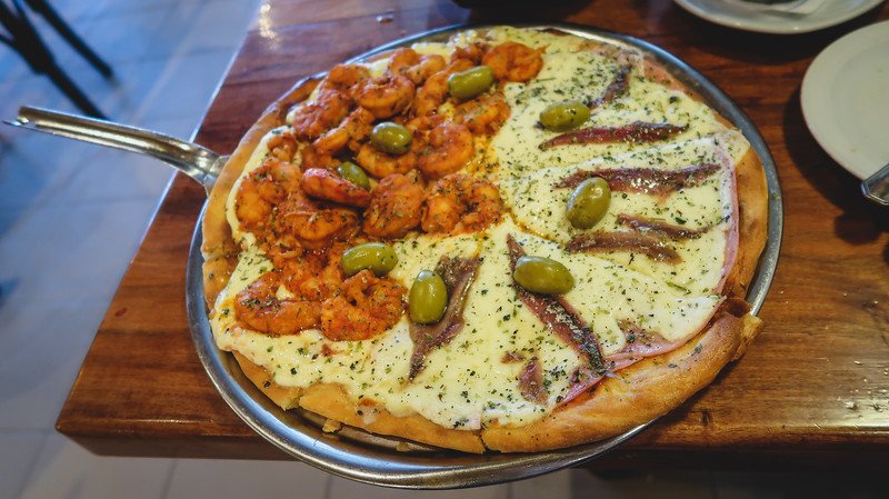 Seafood pizza topped with shrimp, anchovies, and green olives at Chona restaurant in Puerto Madryn, Patagonia, Argentina. A flavorful local specialty combining fresh ingredients from the coast, perfect after exploring Peninsula Valdes
