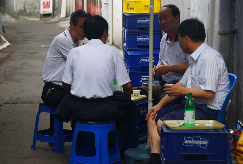 Seoul Korean men sitting on plastic chairs drinking soju in South Korea 