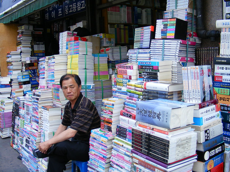 Shopkeeper and his Books in Seoul, South Korea with a mountain of books for sale