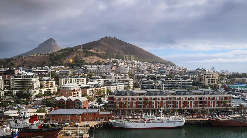 Panoramic view of Signal Hill rising behind the bustling V&A Waterfront in Cape Town, with boats docked in the harbour and historic brick buildings lining the waterfront