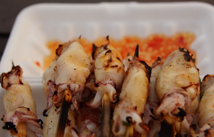 Close-up of freshly grilled squid skewers served on a beachside food stall tray in Sihanoukville, Cambodia, highlighting the coastal city’s vibrant seafood street food culture
