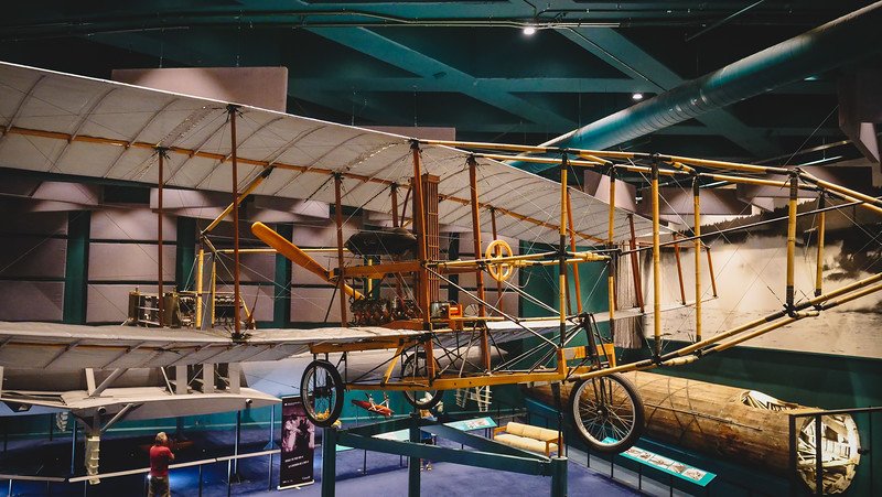A full-scale replica of the Silver Dart aircraft is suspended from the ceiling inside the Alexander Graham Bell National Historic Site in Baddeck, Nova Scotia, showcasing Alexander Graham Bell’s pioneering aviation work during a visit along the Cabot Trail in Cape Breton
