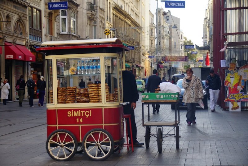 A traditional red street cart selling simit — sesame-crusted Turkish bread rings often compared to pretzels — on a bustling pedestrian street in Istanbul, Turkey