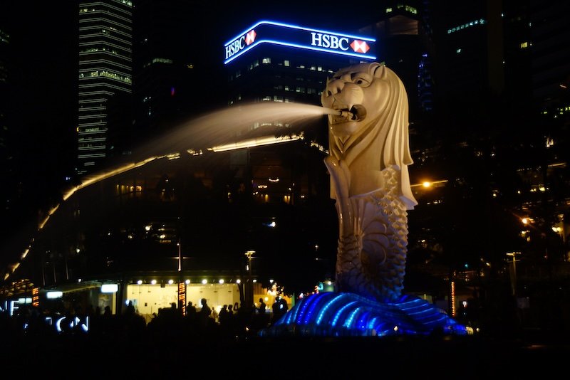 Singapore Merlion spewing water at night with bright lights showcasing modern as of the city in the evening with bright lights aplenty