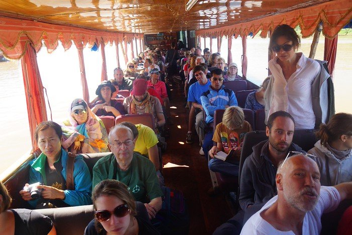 Inside the slow boat to Laos, rows of travelers sit on wooden seats as they journey down the Mekong River toward Luang Prabang. This image shows the ‘good seats’ section near the front of the boat, filled with backpackers and tourists enjoying the scenic ride