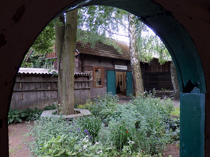 Sorbian homes make up this open air museum in Germany with archway views overlooking flowers and a garden in Spreewald